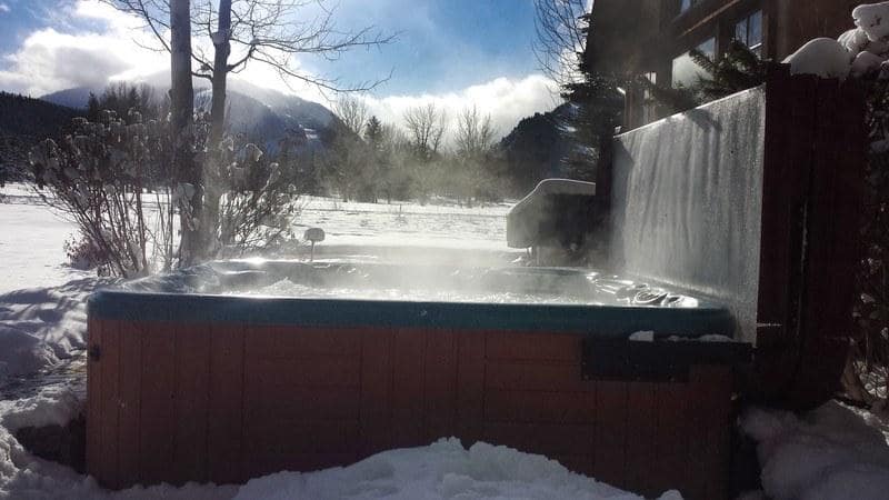 hot tub with opened cover installed in a backyard surrounded by snow